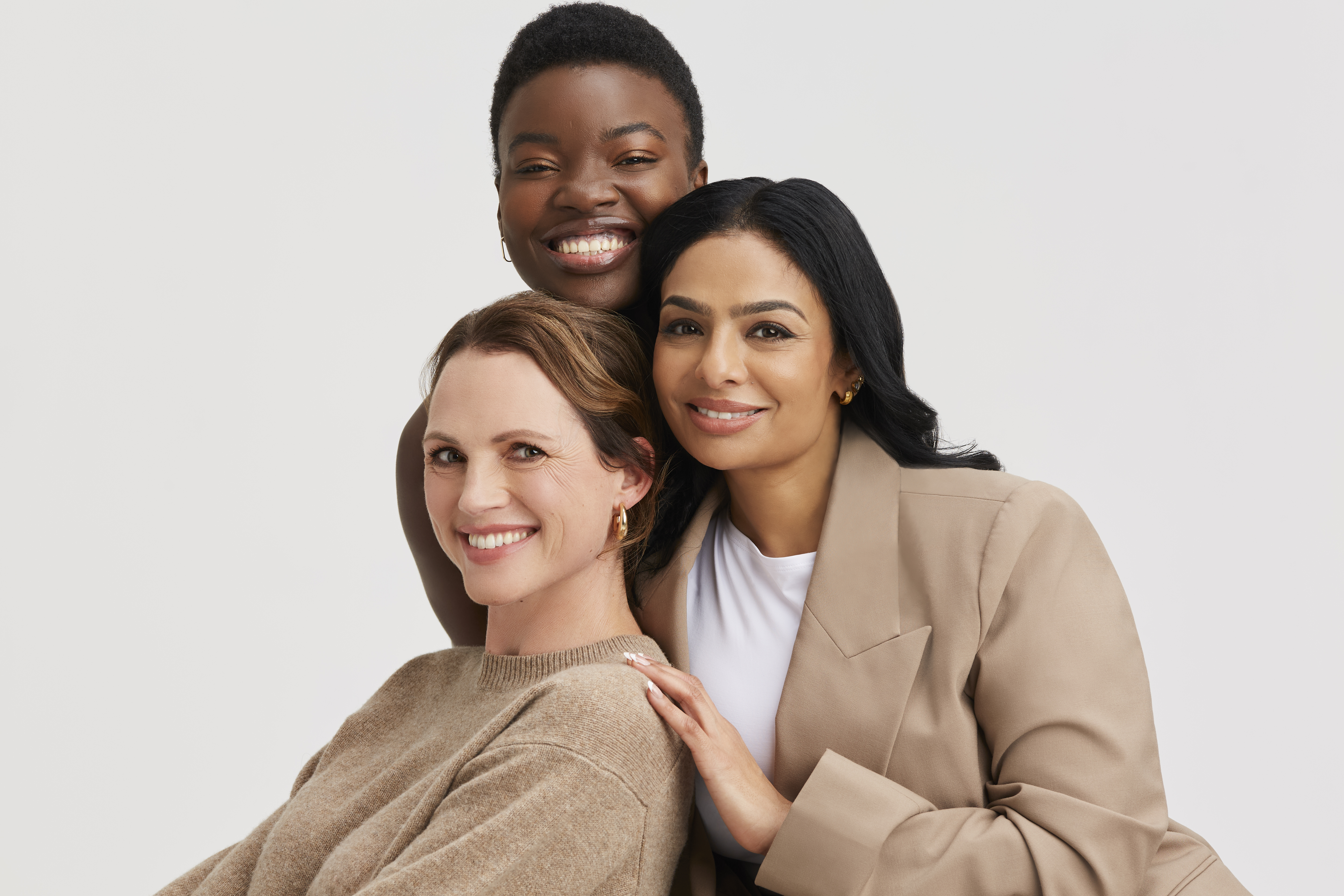 Three diverse women smiling, embracing each other.