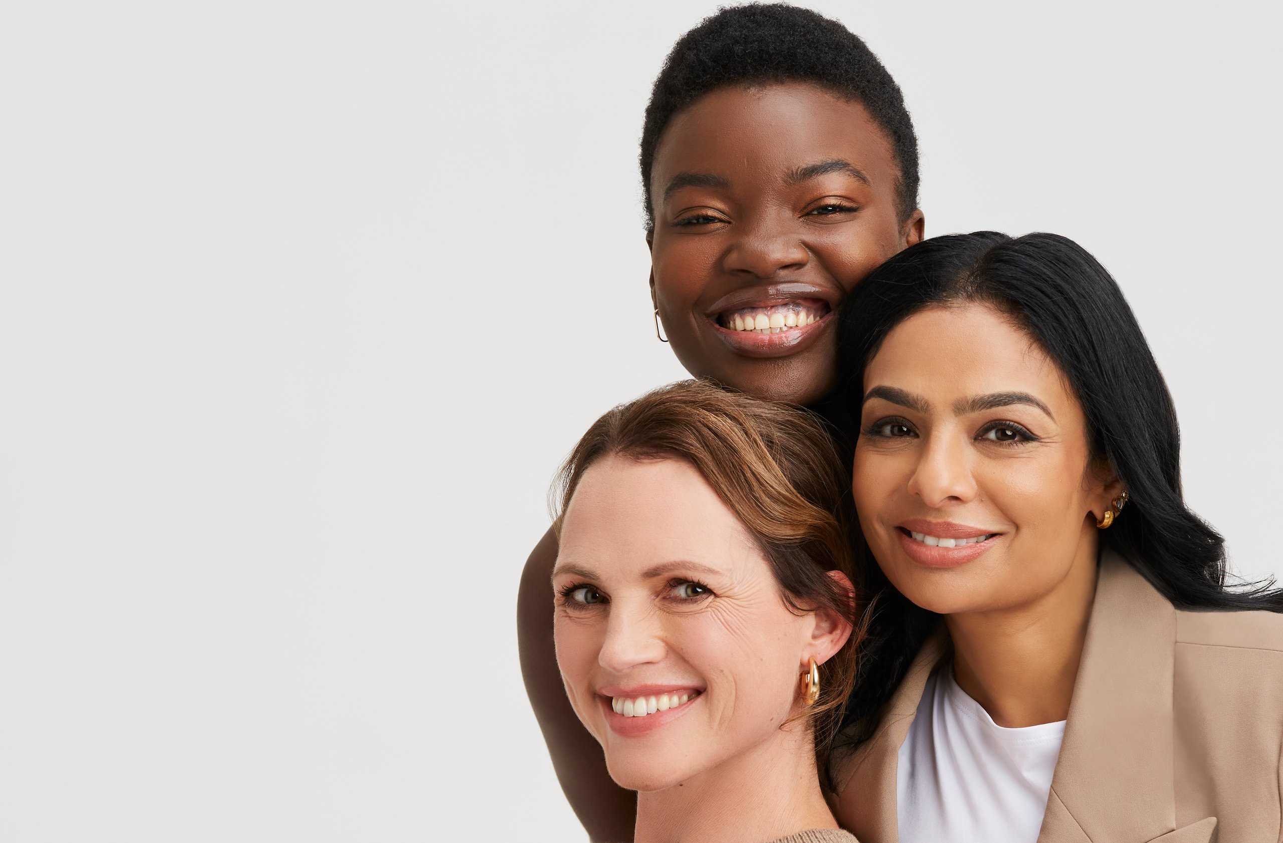Three diverse women smiling, embracing each other.