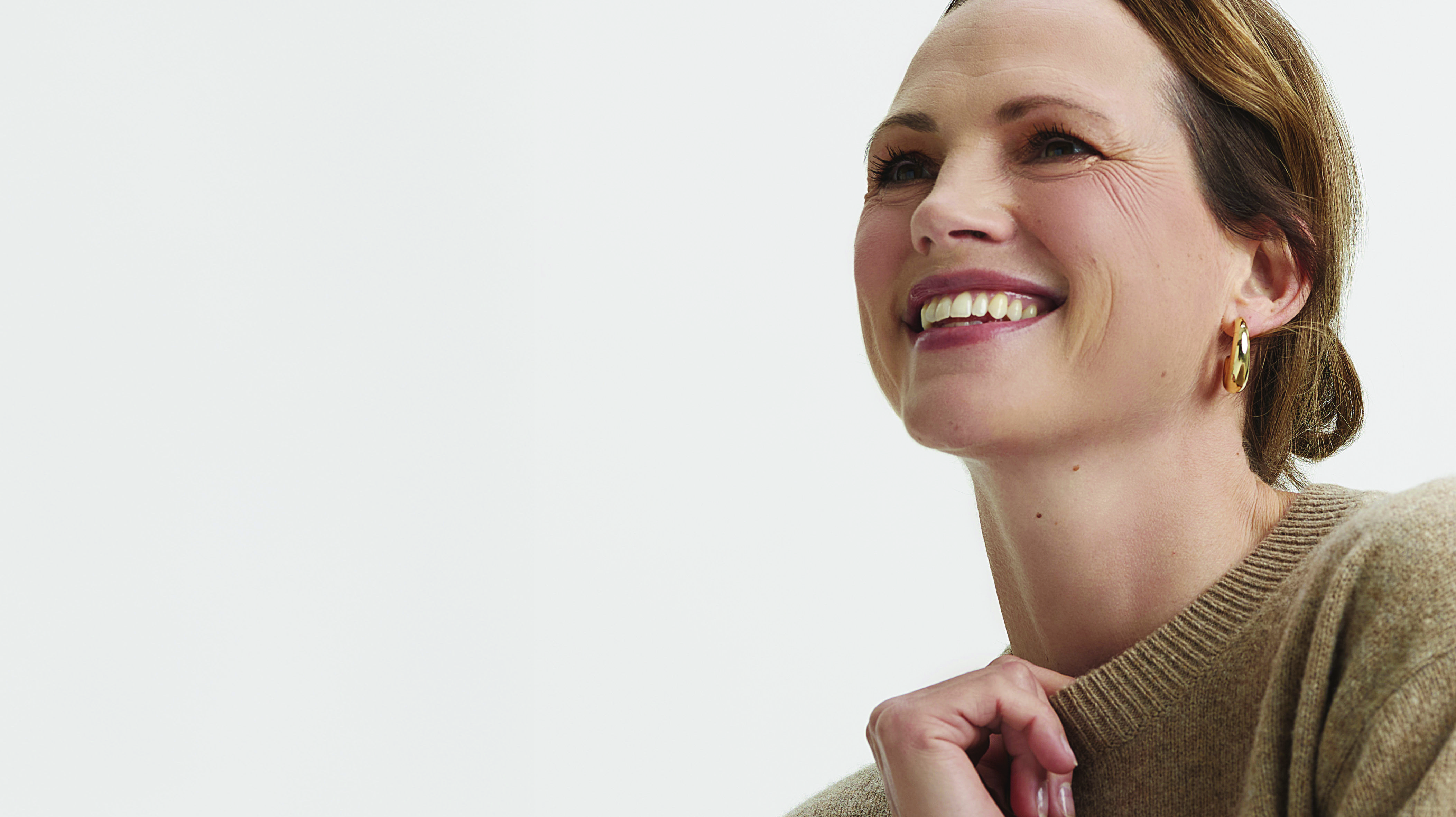 Woman in a beige sweater smiling, with gold earrings.