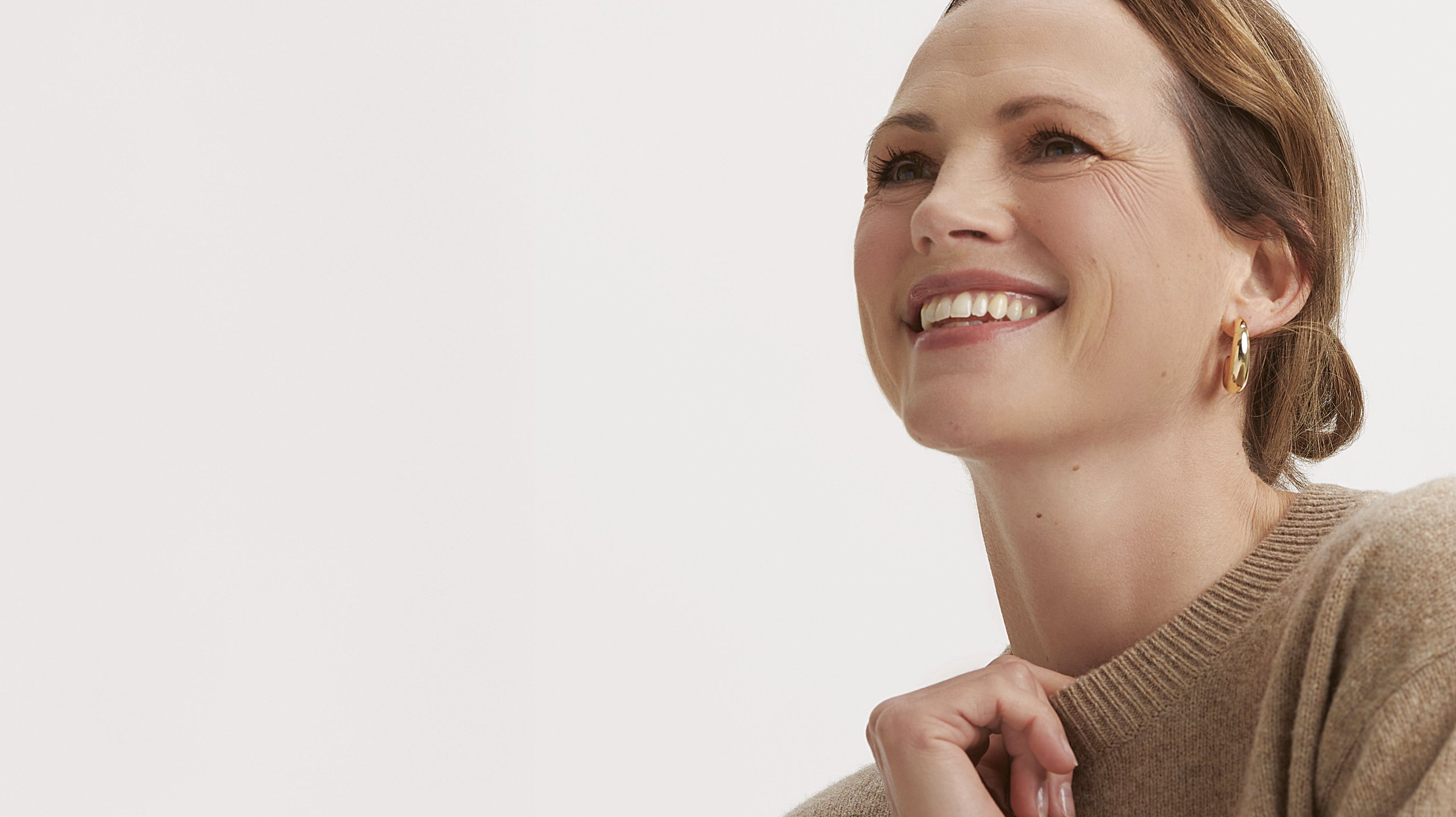 Woman in a beige sweater smiling, with gold earrings.