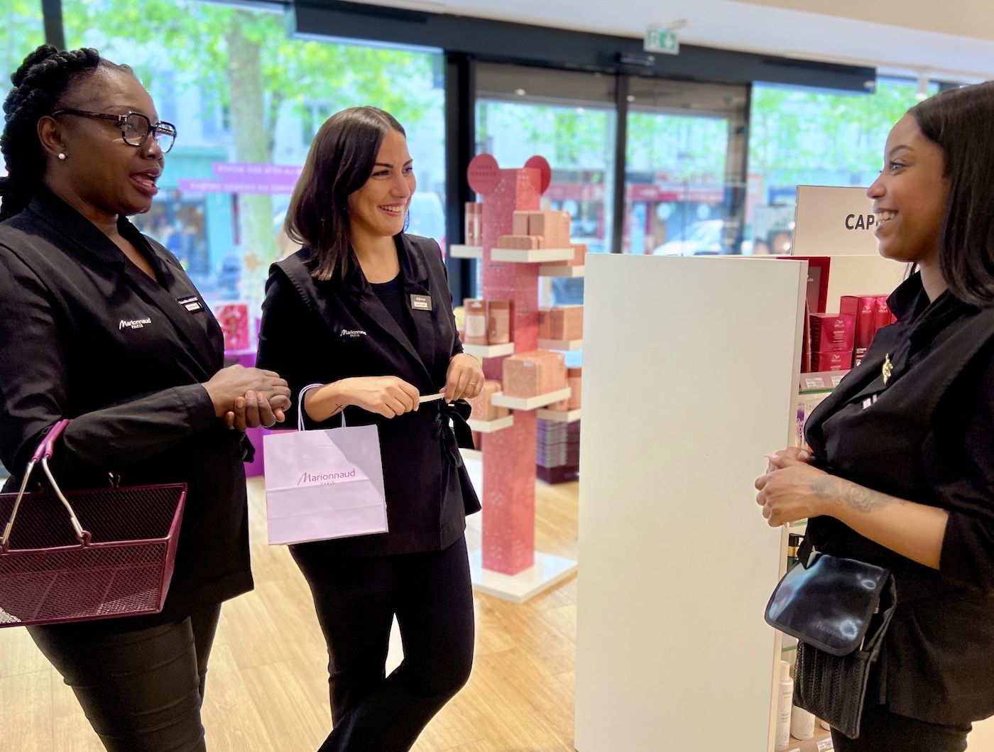 Three women in a Marionnaud store, smiling and talking. One holding a basket.