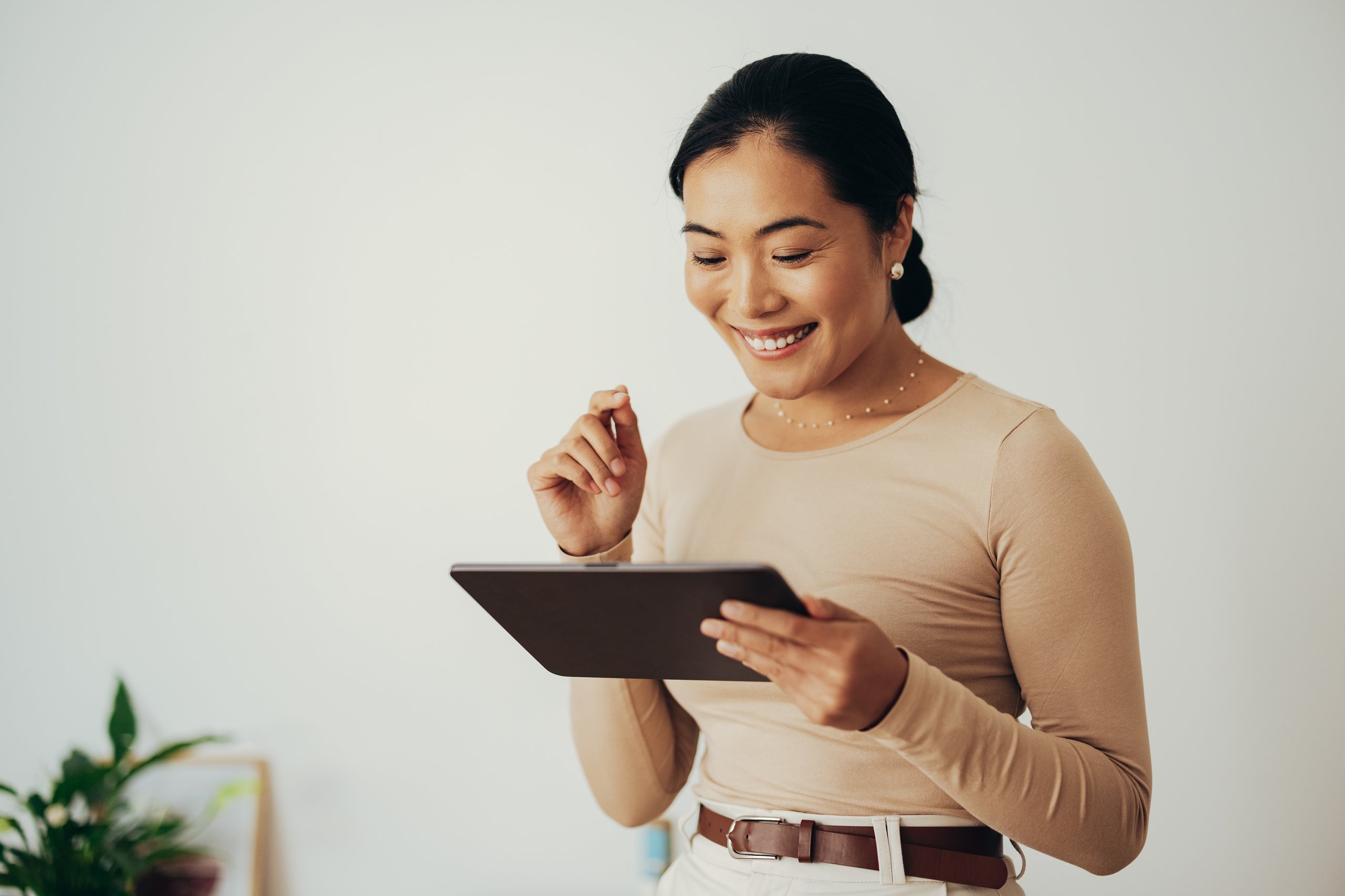 Smiling woman using a tablet, wearing a beige shirt and white pants.